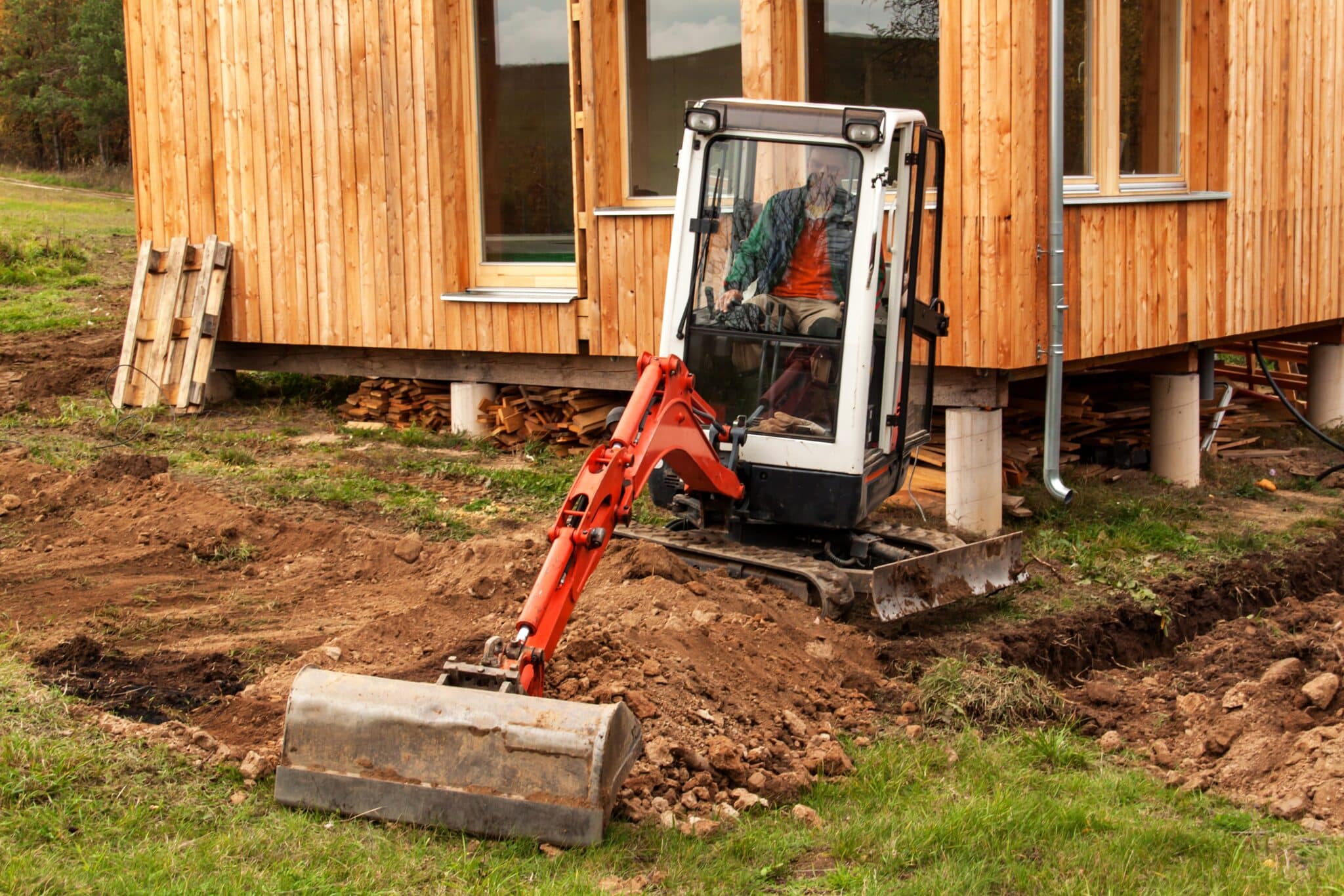 Work on the construction site of an ecological house. The excavator adjusts the terrain. A small digger in the garden